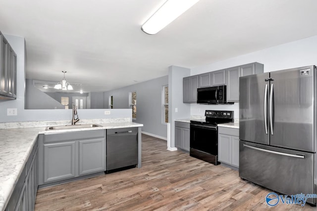 kitchen featuring black appliances, sink, hanging light fixtures, gray cabinetry, and a chandelier