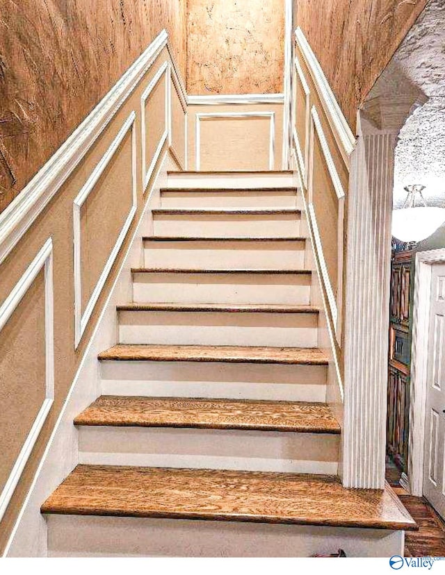 staircase featuring wainscoting and a decorative wall