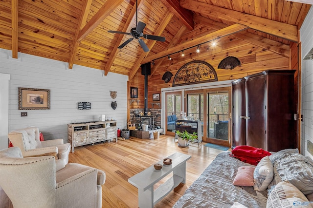 living room with wood finished floors, beam ceiling, a wood stove, wood ceiling, and wood walls