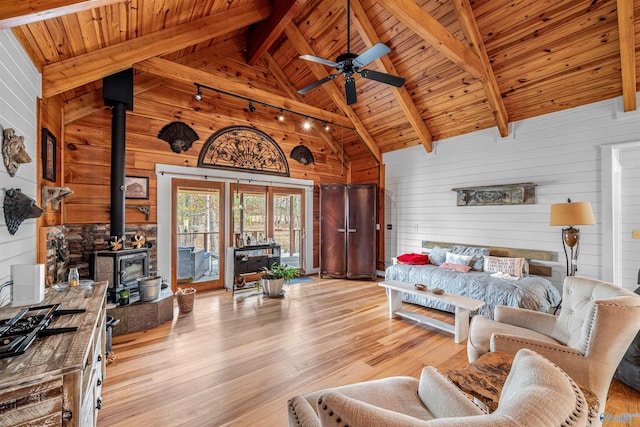 living area featuring beamed ceiling, wooden ceiling, a wood stove, light wood-style floors, and high vaulted ceiling