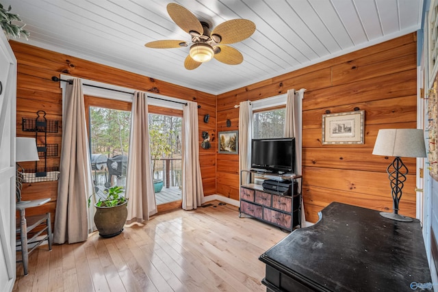 living room with light wood-type flooring, wooden ceiling, wood walls, and a ceiling fan