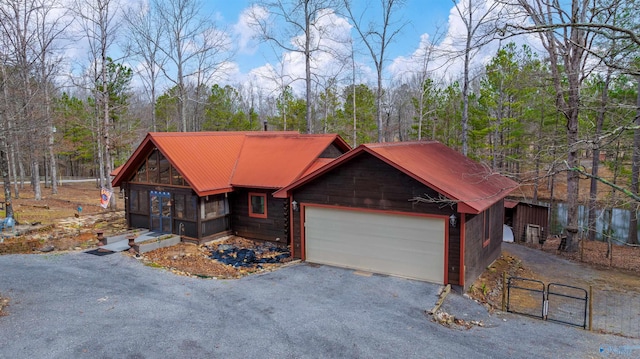 chalet / cabin with aphalt driveway, an attached garage, metal roof, and a gate