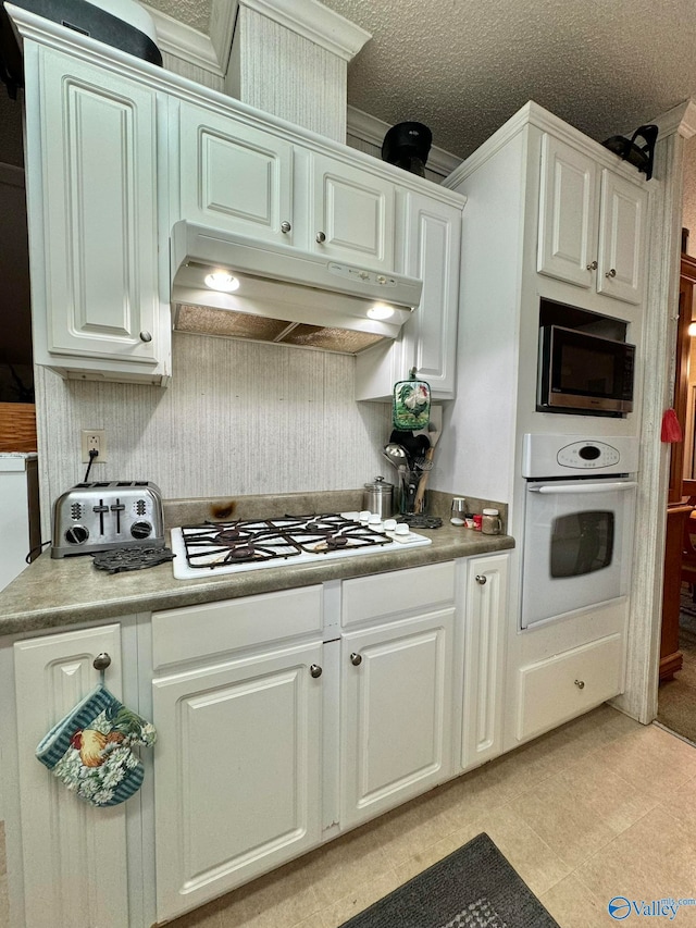 kitchen featuring a textured ceiling, ornamental molding, white appliances, and white cabinetry