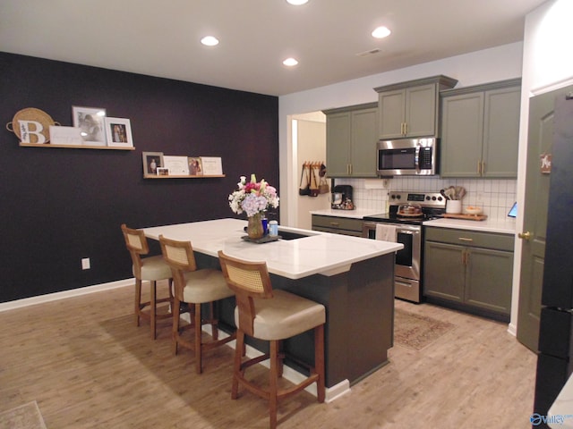 110 Oak Path Ln, Harvest, AL 35749 - kitchen featuring appliances with stainless steel finishes, a kitchen island with sink, light wood-style flooring, recessed lighting, and backsplash