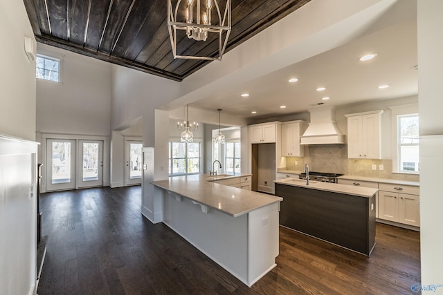 kitchen with dark wood-style flooring, a spacious island, custom range hood, tasteful backsplash, and an inviting chandelier