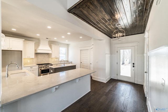 kitchen with stainless steel stove, custom exhaust hood, dark wood-style floors, tasteful backsplash, and a center island with sink