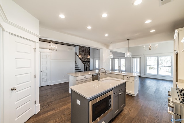 kitchen featuring a center island with sink, visible vents, stainless steel microwave, dark wood-style flooring, and a sink