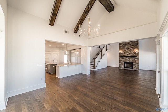 unfurnished living room with high vaulted ceiling, a fireplace, stairs, dark wood finished floors, and an inviting chandelier