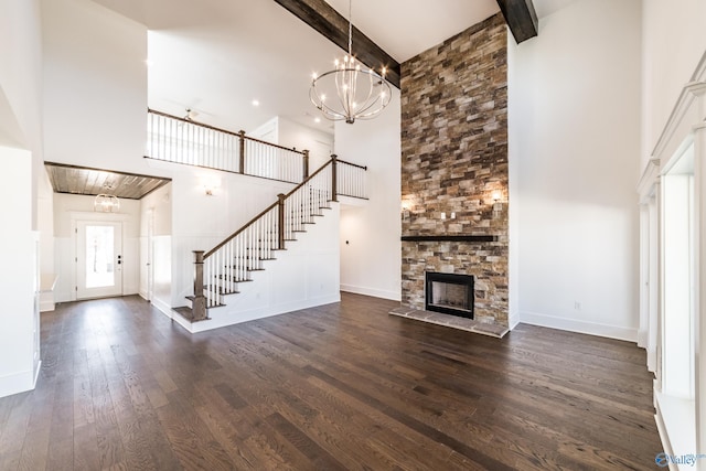 unfurnished living room with dark wood finished floors, an inviting chandelier, stairs, a fireplace, and beam ceiling