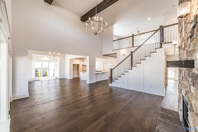 unfurnished living room featuring stairway, a chandelier, dark wood-style flooring, and a stone fireplace