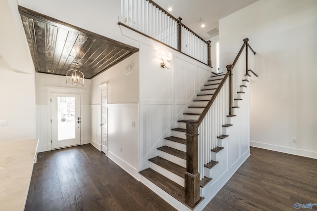 entrance foyer with visible vents, a wainscoted wall, dark wood-type flooring, an inviting chandelier, and stairs