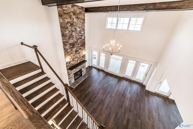 unfurnished living room featuring dark wood finished floors, a fireplace, a notable chandelier, stairway, and a towering ceiling