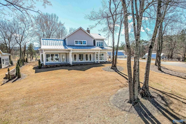 view of front of house featuring metal roof, covered porch, a front yard, a standing seam roof, and a chimney