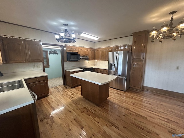 kitchen with an inviting chandelier, light wood-style floors, a sink, black microwave, and stainless steel fridge