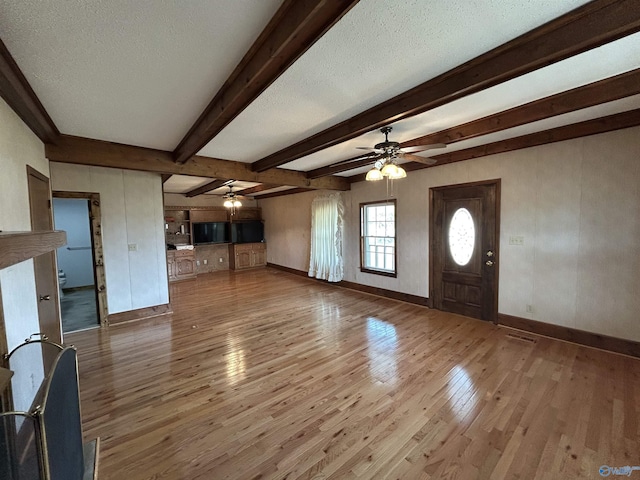 unfurnished living room with baseboards, beamed ceiling, a textured ceiling, and hardwood / wood-style floors