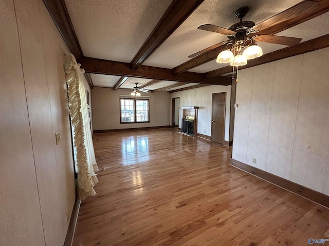 unfurnished living room with ceiling fan, a textured ceiling, wood finished floors, beamed ceiling, and baseboards