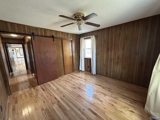 unfurnished bedroom featuring light wood-style flooring, wooden walls, and a textured ceiling