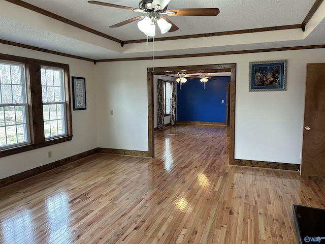 empty room featuring a raised ceiling, ornamental molding, light wood-style floors, a textured ceiling, and baseboards