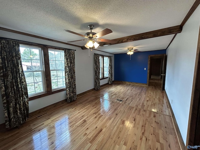 spare room featuring light wood-type flooring, visible vents, baseboards, and a textured ceiling