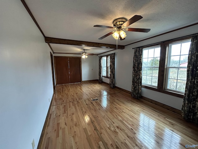 empty room with light wood finished floors, baseboards, ornamental molding, a textured ceiling, and beam ceiling