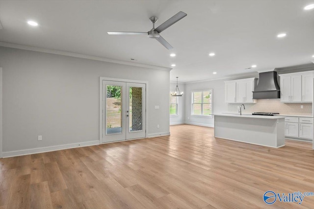 kitchen with light wood-type flooring, custom exhaust hood, ceiling fan with notable chandelier, ornamental molding, and white cabinetry