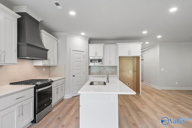 kitchen with white cabinets, custom exhaust hood, stainless steel appliances, sink, and a center island with sink