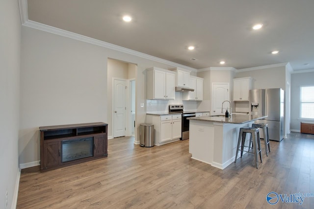 kitchen featuring a breakfast bar, light wood-style flooring, appliances with stainless steel finishes, a sink, and under cabinet range hood