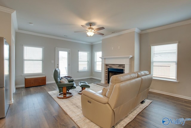 living room with ornamental molding, a stone fireplace, wood finished floors, and baseboards