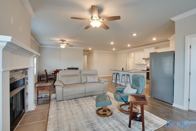 living area with a stone fireplace, recessed lighting, wood finished floors, baseboards, and ornamental molding