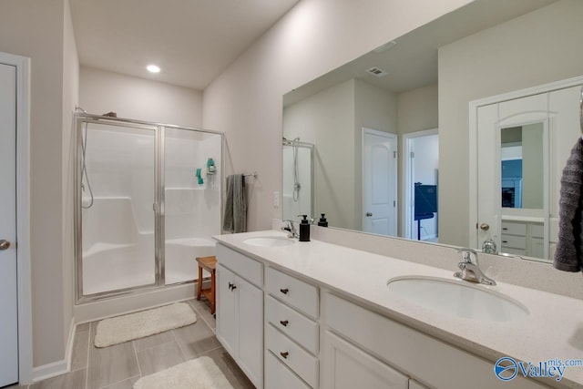 full bathroom featuring double vanity, a shower stall, a sink, and recessed lighting