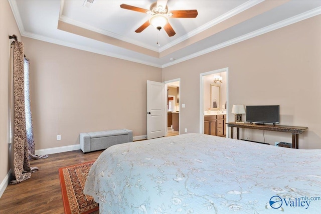 bedroom featuring wood finished floors, a tray ceiling, baseboards, crown molding, and connected bathroom