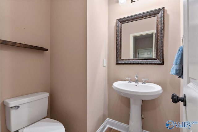 half bath with toilet, a sink, and baseboards
