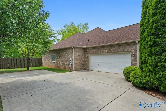 view of side of property featuring fence, concrete driveway, roof with shingles, and brick siding