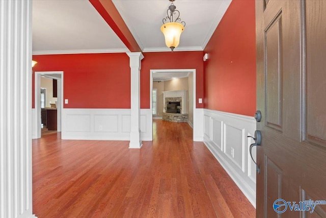 foyer entrance with ornate columns, crown molding, a stone fireplace, wood finished floors, and wainscoting