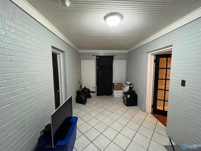 hallway with light tile patterned floors, brick wall, and ornamental molding