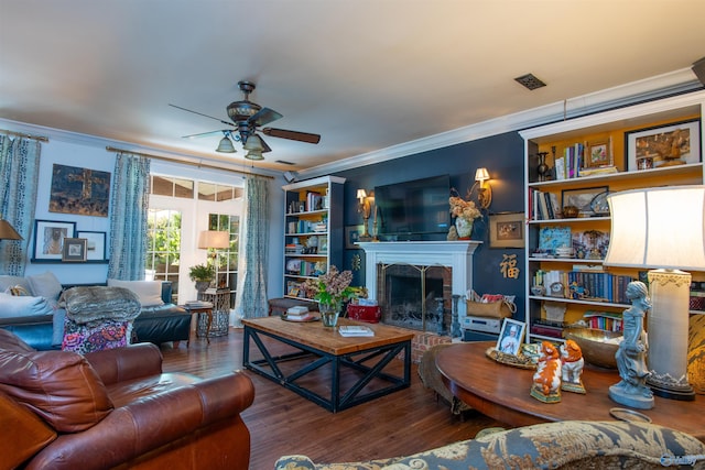 living area with visible vents, a ceiling fan, ornamental molding, wood finished floors, and a fireplace