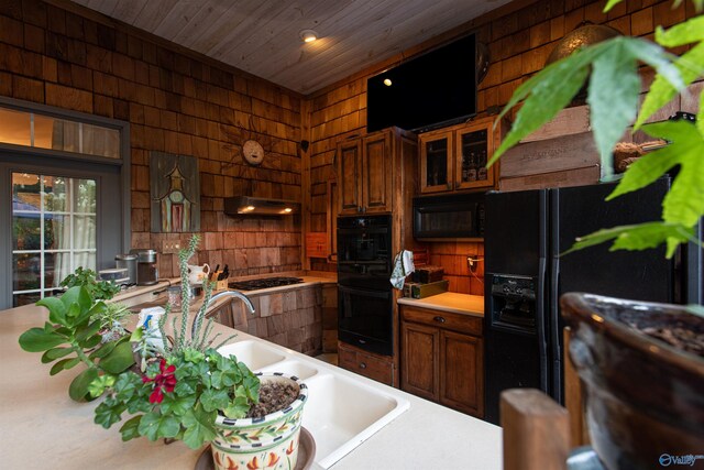 kitchen with light countertops, wood ceiling, wooden walls, under cabinet range hood, and black appliances