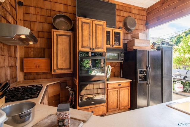 kitchen with glass insert cabinets, brown cabinets, light countertops, wood walls, and black appliances