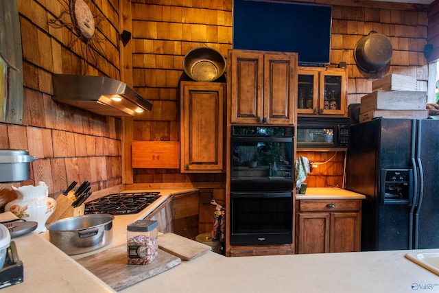 kitchen with brown cabinets, light countertops, glass insert cabinets, under cabinet range hood, and black appliances