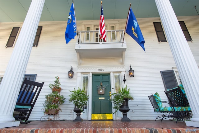 view of exterior entry with covered porch and a balcony