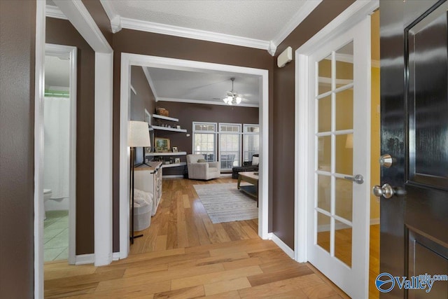 hall with ornamental molding, a textured ceiling, light wood-type flooring, and french doors