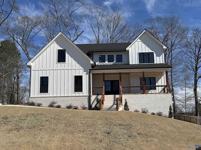 modern farmhouse featuring brick siding, roof with shingles, covered porch, board and batten siding, and a front yard