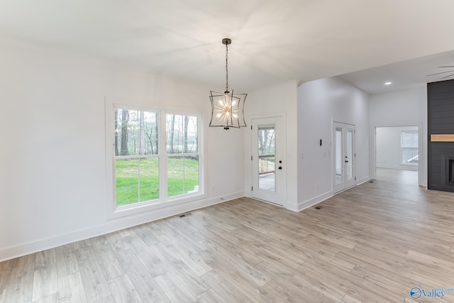 unfurnished dining area with light wood-style flooring, a notable chandelier, a large fireplace, visible vents, and baseboards