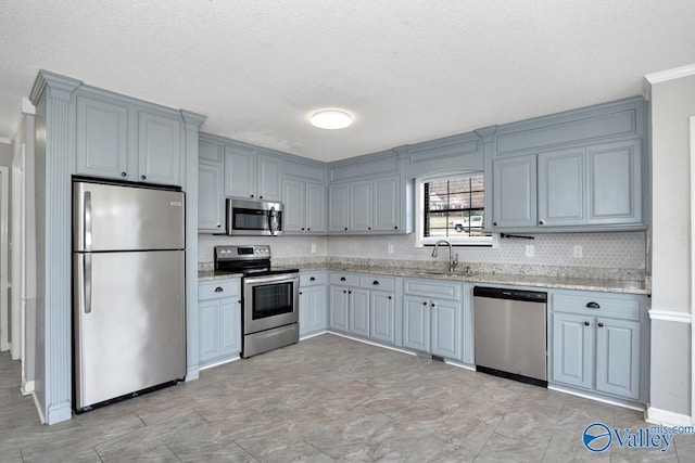 kitchen with light stone counters, appliances with stainless steel finishes, sink, and backsplash