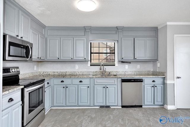 kitchen featuring sink, light stone counters, appliances with stainless steel finishes, gray cabinets, and backsplash