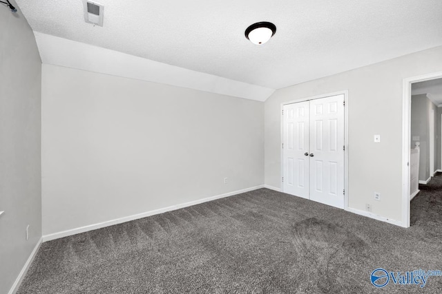 unfurnished bedroom with vaulted ceiling, a closet, a textured ceiling, and dark colored carpet