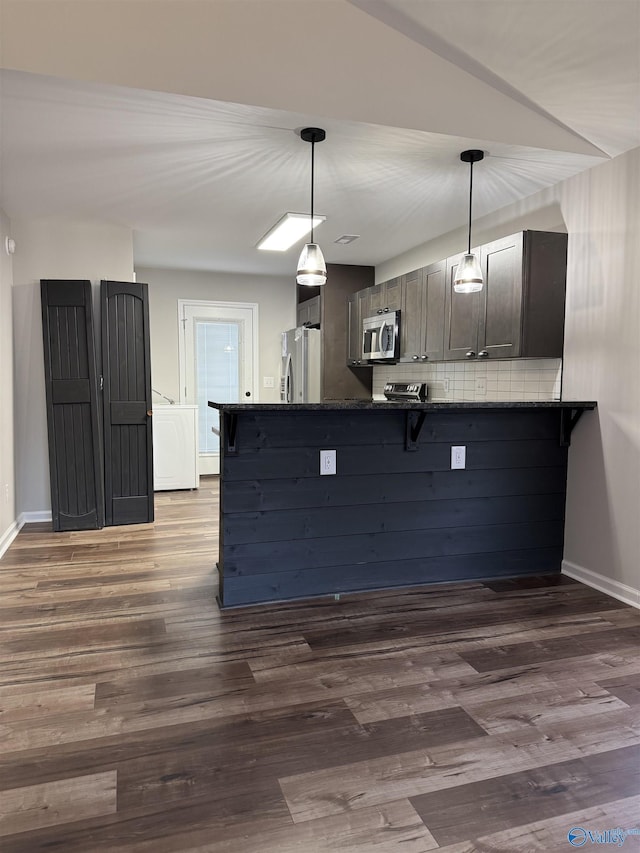 kitchen featuring backsplash, appliances with stainless steel finishes, hanging light fixtures, washer / dryer, and dark wood-style flooring