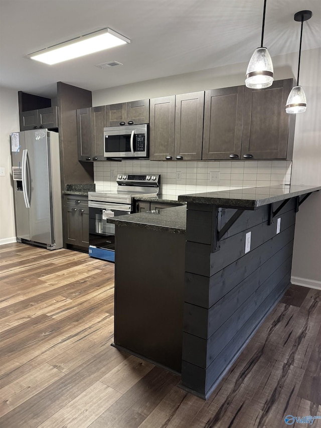 kitchen with backsplash, a breakfast bar area, appliances with stainless steel finishes, light wood-type flooring, and dark stone countertops