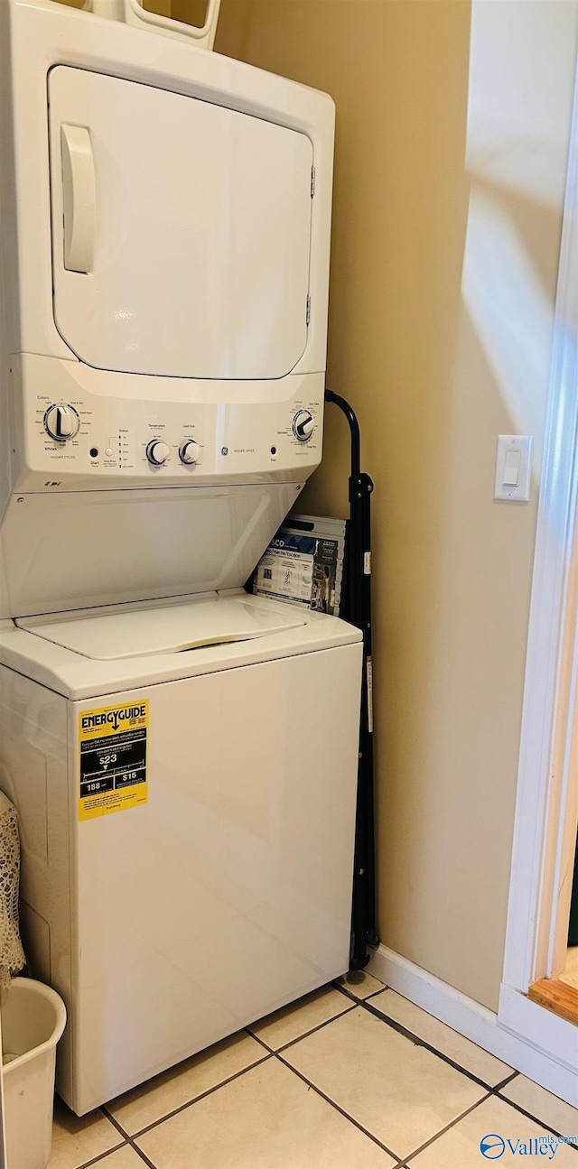 clothes washing area with stacked washer / dryer, laundry area, baseboards, and light tile patterned floors