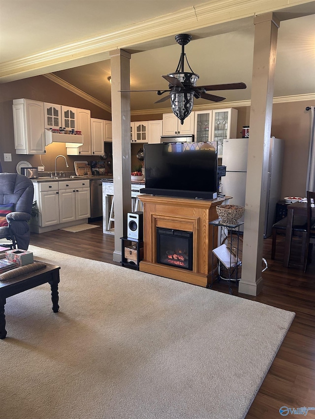 living room featuring dark wood-style flooring, ornamental molding, a ceiling fan, vaulted ceiling, and a warm lit fireplace